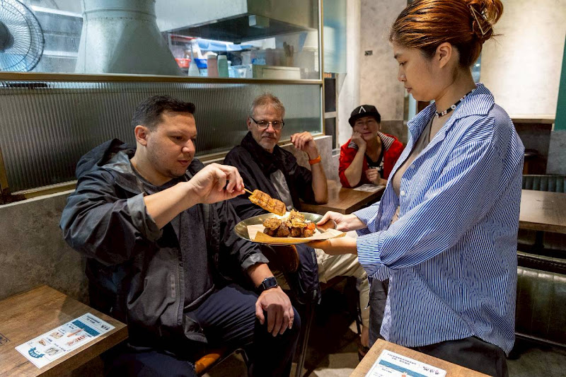 Tourists enjoying authentic Taiwanese charcoal grilled snacks at a local Izakaya with Kunji